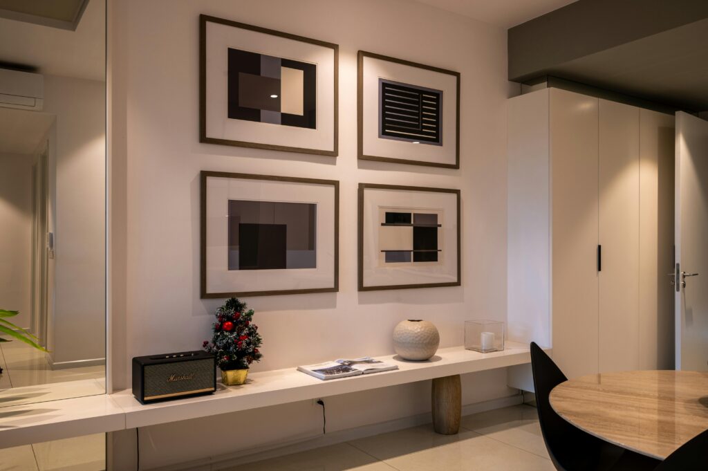 A modern interior gallery wall featuring four large , dark wood custom frames with matted abstract art, arranged in a grid above a minimalist white console bench.