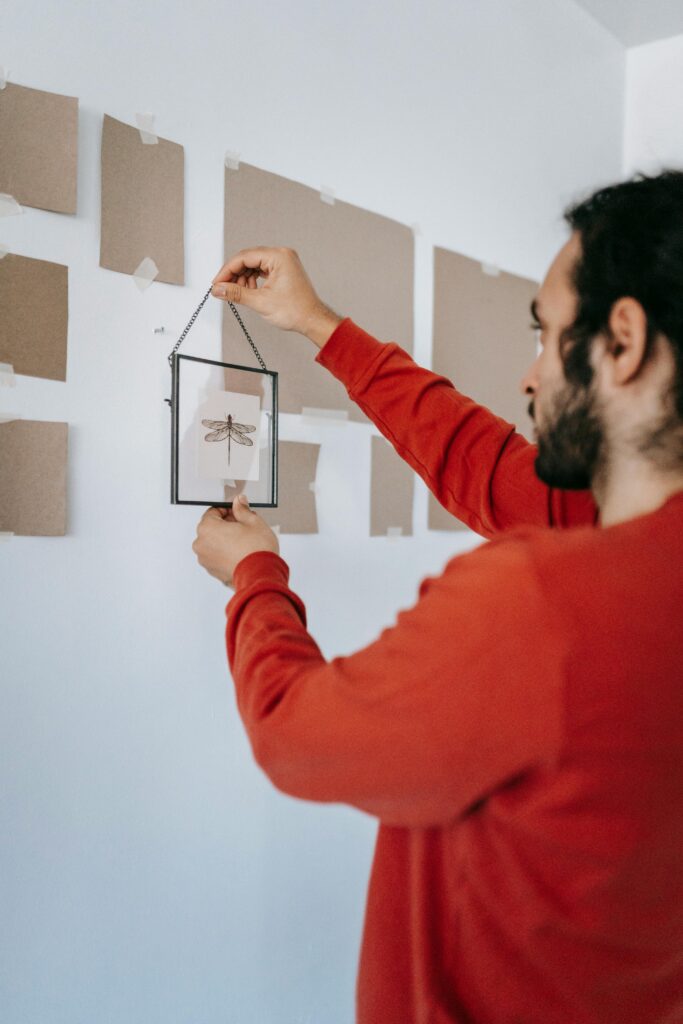 A professional installer carefully hanging a framed artwork over paper templates on a wall layout.